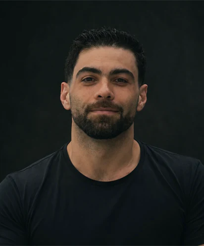Renan Fraga, personal trainer, de camiseta preta e barba, em fundo escuro.